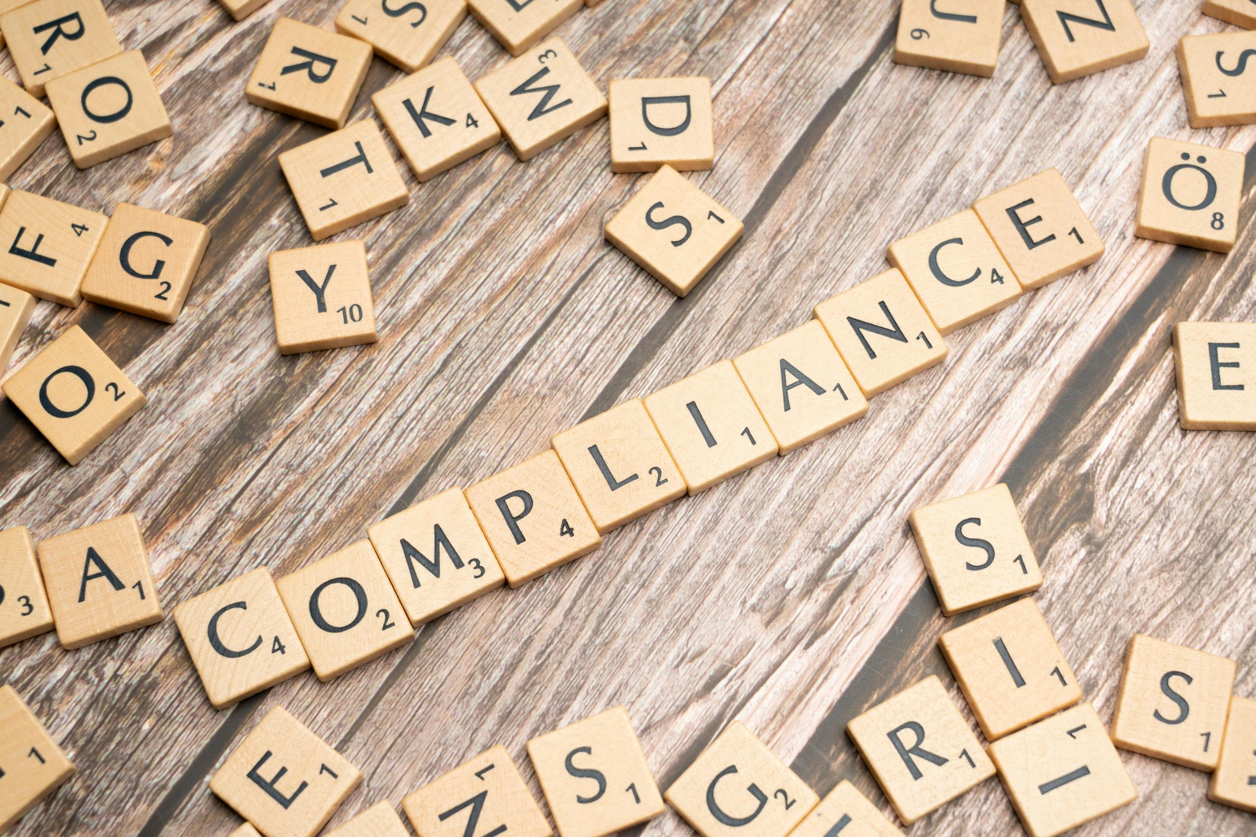 Scrabble tiles spelling the word compliance on a wooden background