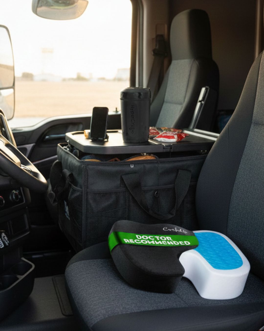 Truck cab interior with seat cushion, mobile workstation, travel organizer, and coffee mug setup for driver comfort.